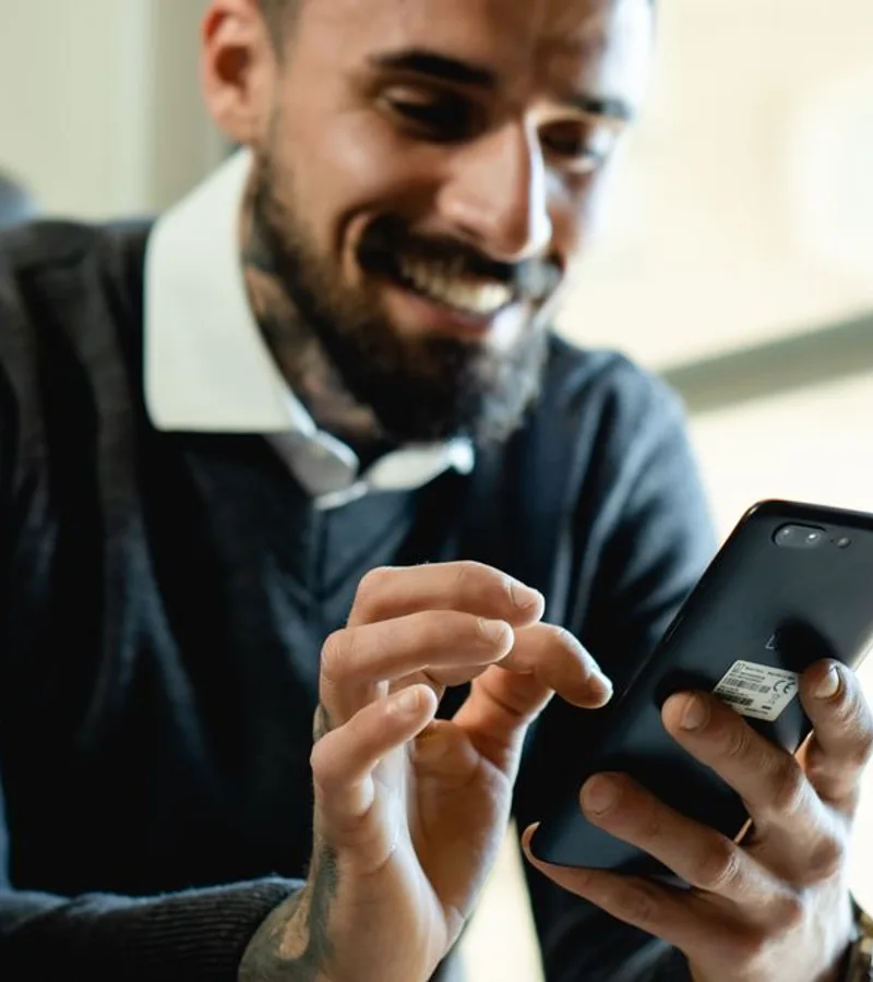 Homem sorrindo enquanto usa o celular em uma situação do dia a dia